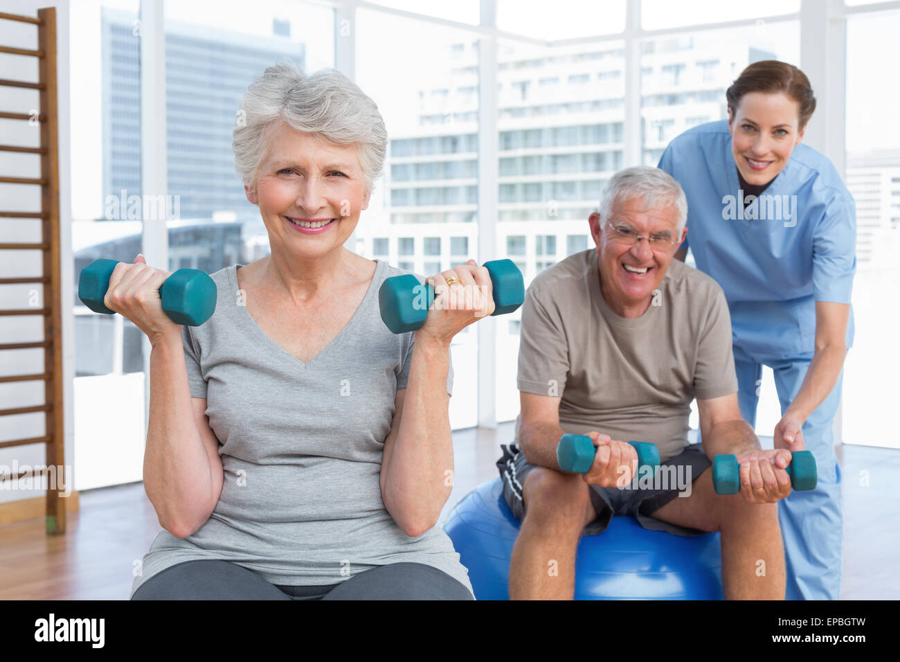 Female therapist aider senior couple with dumbbells Banque D'Images