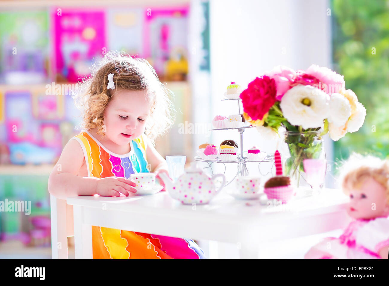 Adorable bébé fille avec des cheveux bouclés portant une robe colorée pour  son anniversaire jouer tea party avec une poupée, des plats de jouets Photo  Stock - Alamy
