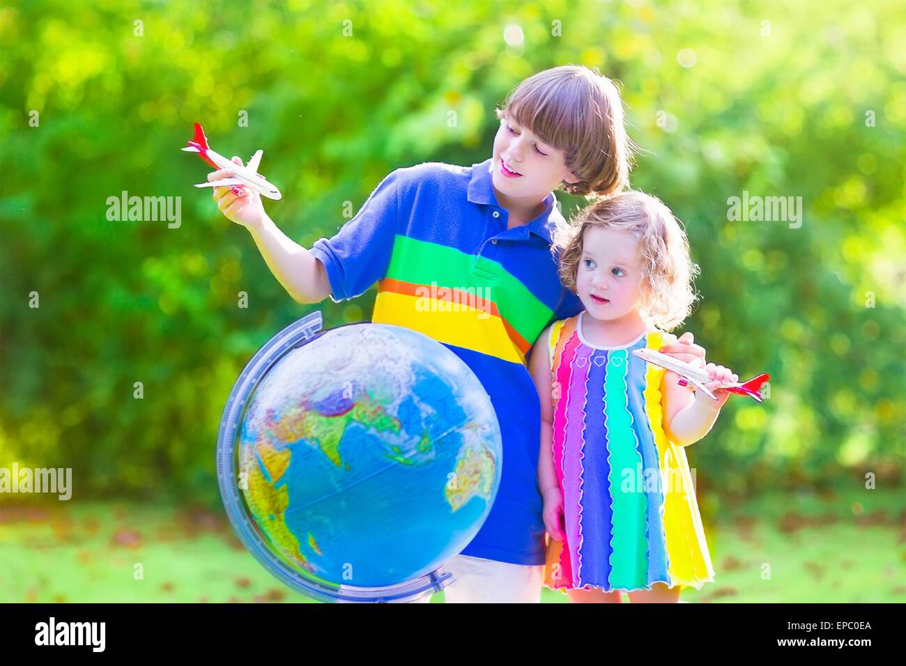 Deux enfants heureux, cute girl bouclés et un sourire l'âge scolaire boy playing with toy des avions volant dans le monde Banque D'Images