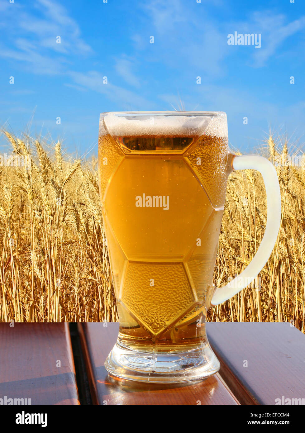 Verre de bière sur la table en bois contre les épis de blé d'or et bleu ciel. Banque D'Images