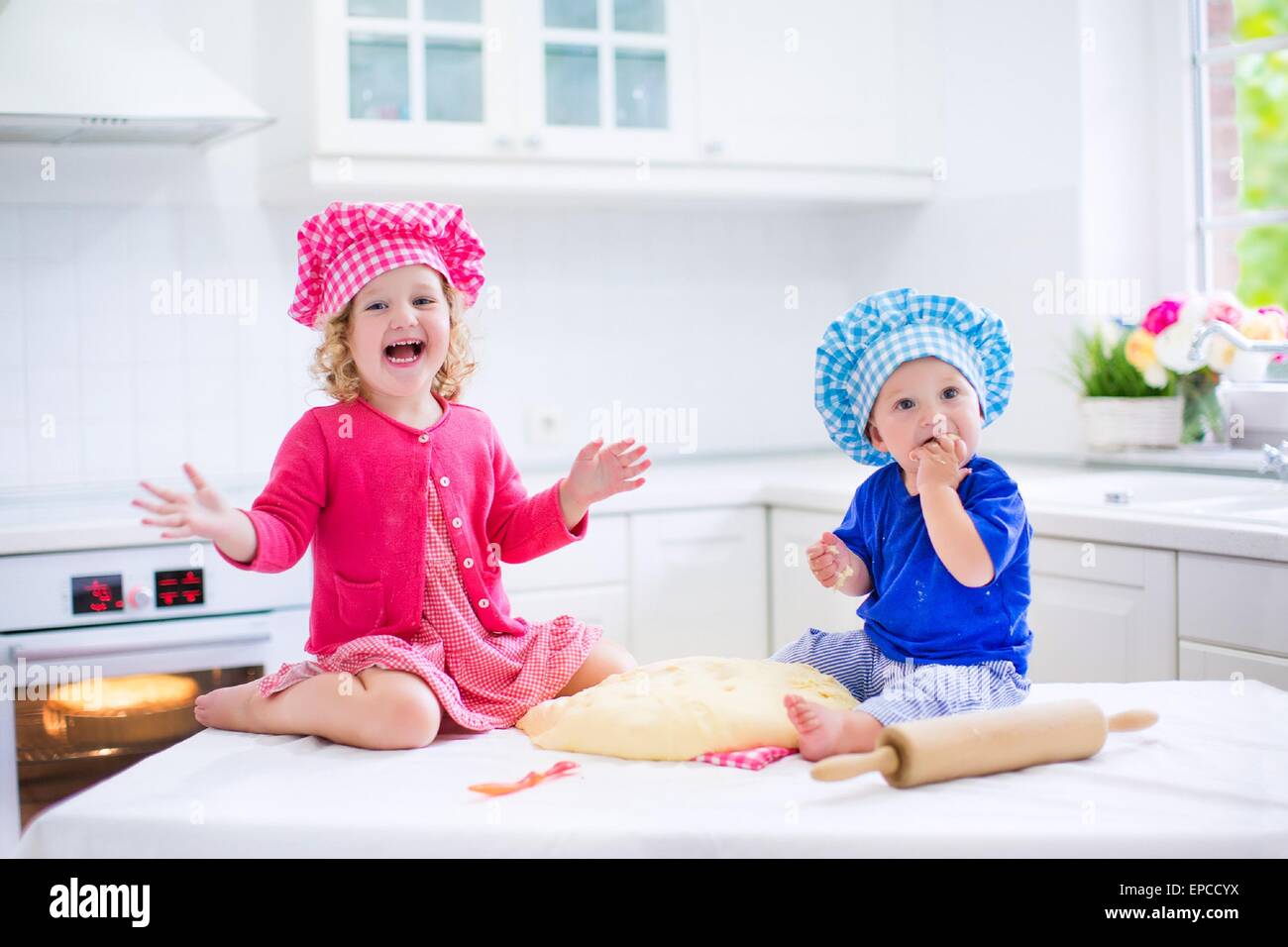 Enfants mignon, adorable petite fille et funny baby boy wearing rose et bleu de chef de jouer avec la pâte à tarte à la cuisson d'une cuisine Banque D'Images