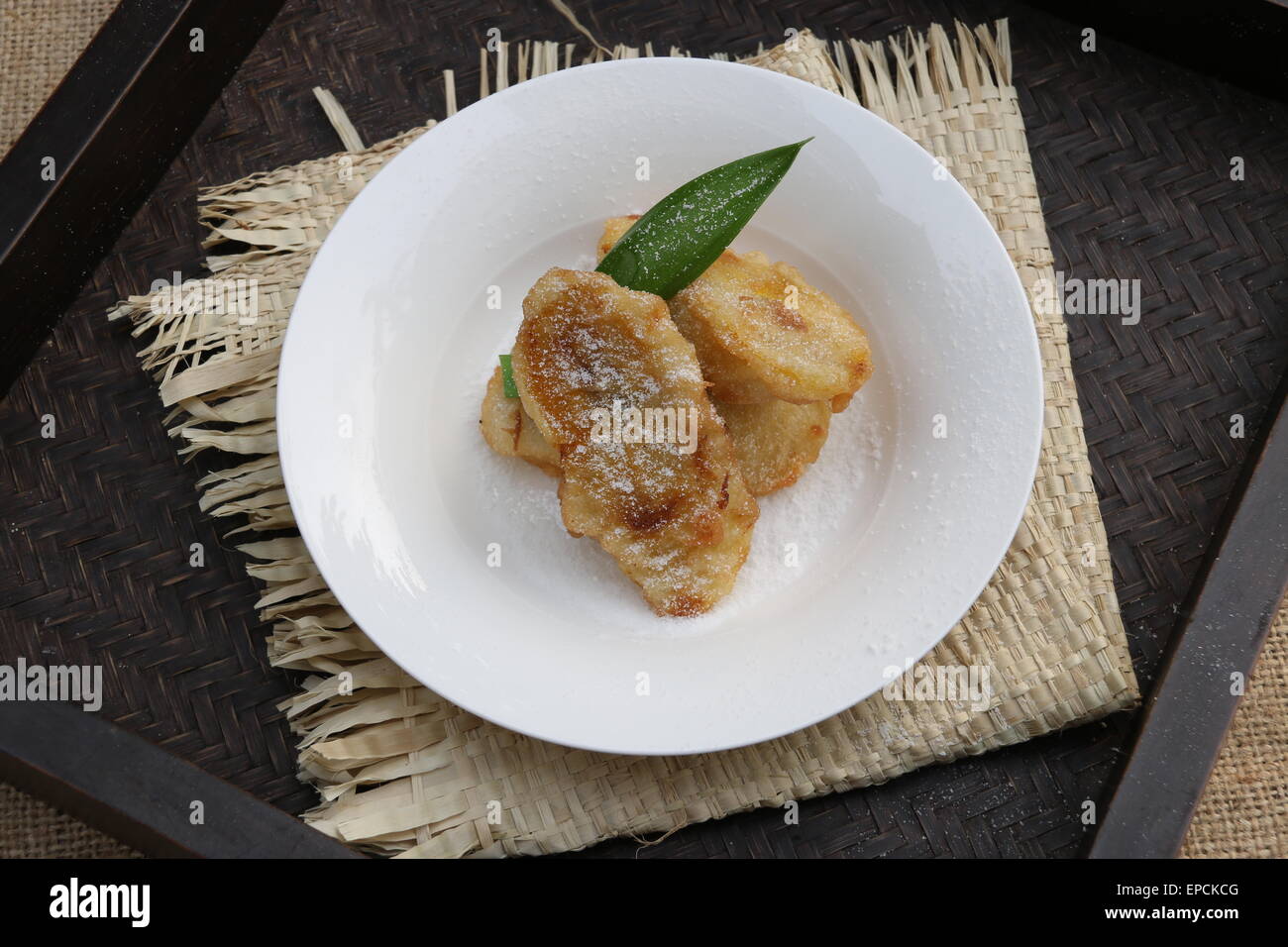 Trois morceaux de pâte-bananes frites avec du sucre en poudre blanc sur plaque. Sur le plateau de bambou tressé et matelas de paille Banque D'Images