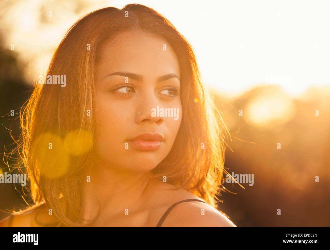 Portrait lumineux avec des reflets d'une jeune femme les yeux dans la distance un jour d'été alors que le soleil se couche derrière elle. Banque D'Images
