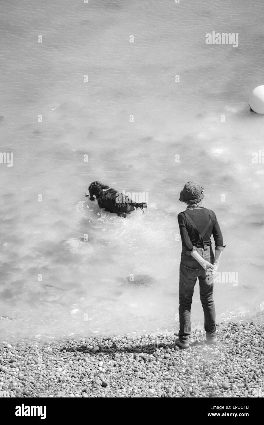 Femme debout sur la plage jouant avec un chien dans l'infrarouge à Freshwater Bay, île de Wight, Hampshire Royaume-Uni en mai Banque D'Images