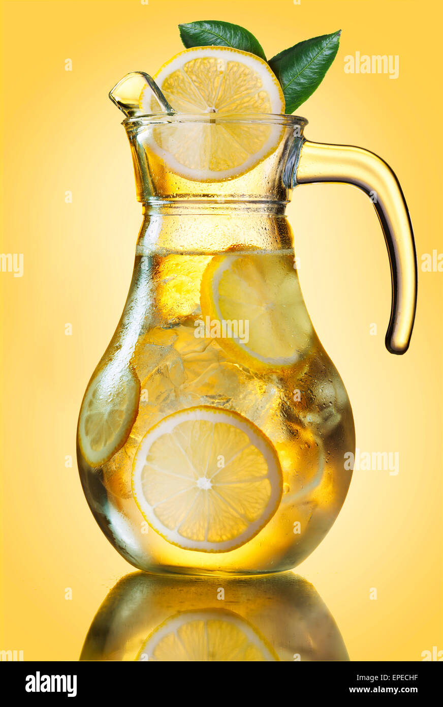 Embuées lemonade pitcher de tranches de citron et des glaçons décoré de feuilles sur jaune. Banque D'Images