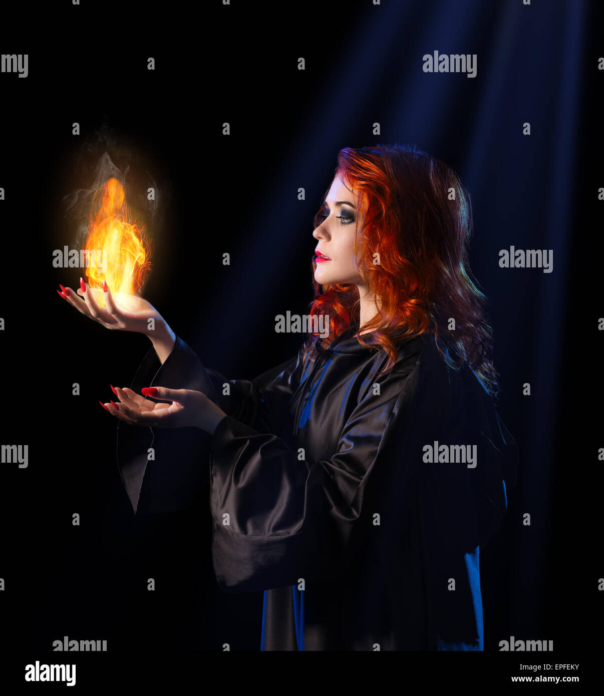 Jeune sorcière avec flamme sur fond de rayons bleu Banque D'Images