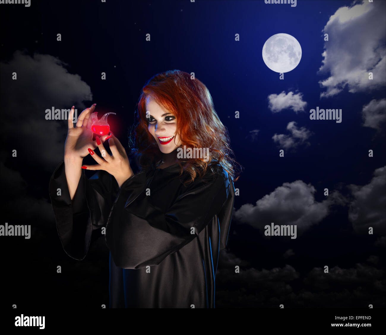 Jeune sorcière avec potion rouge sur fond de ciel de nuit Banque D'Images