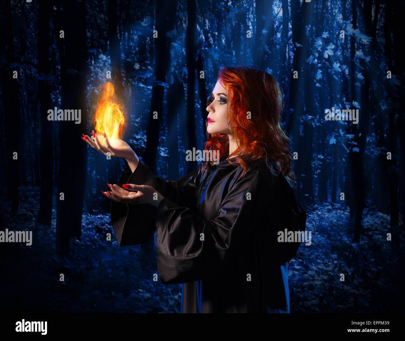 Jeune sorcière dans la nuit dans la forêt clair de lune avec la flamme Banque D'Images