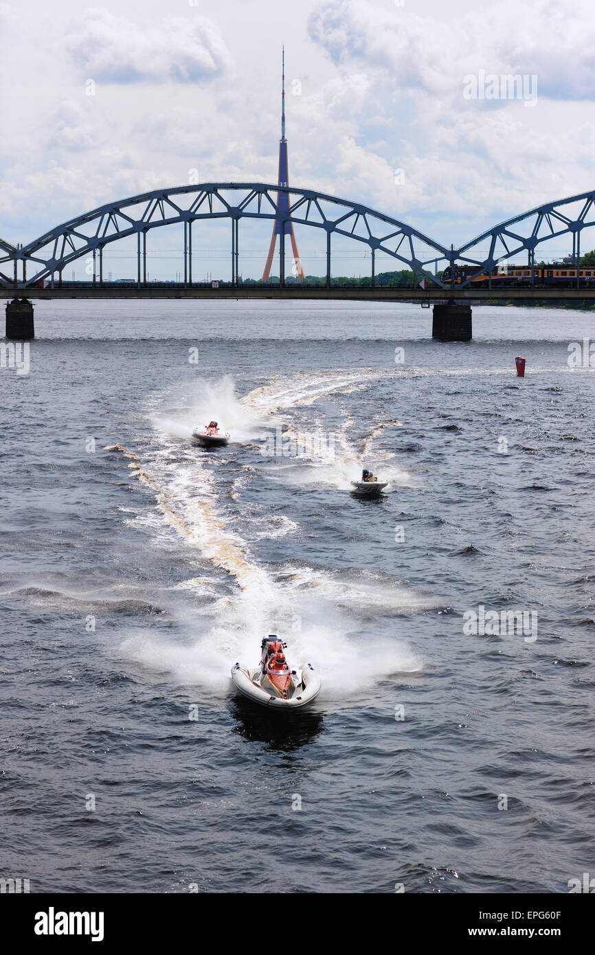 Bateaux à moteur à grande vitesse sur la Daugava à Riga sur l'arrière-plan de train sur le pont et une tour de la télévision Banque D'Images