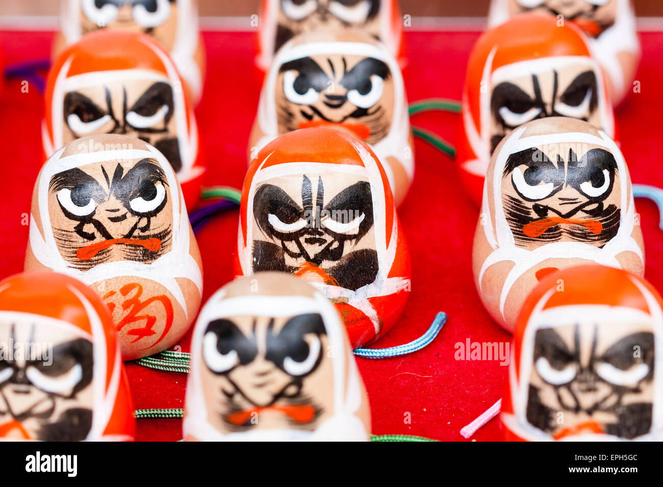 Gros plan de quatre rangées de visages de poupée de paper-maché rouge Daruma à vendre au temple de Suma-dera à Suma, Kobe. Ils représentent le visage d'un homme barbu. Banque D'Images