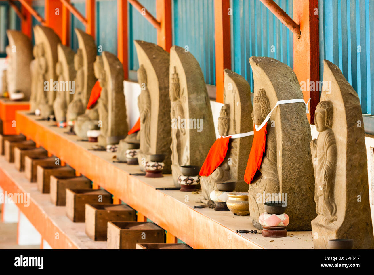 Vue le long d'une rangée de statues rouges de Jizo Bosatsu sur le pas de vermillon. Chaque statue a un petit bol laissé devant lui avec bâton de choc pour sonner. Japon. Banque D'Images