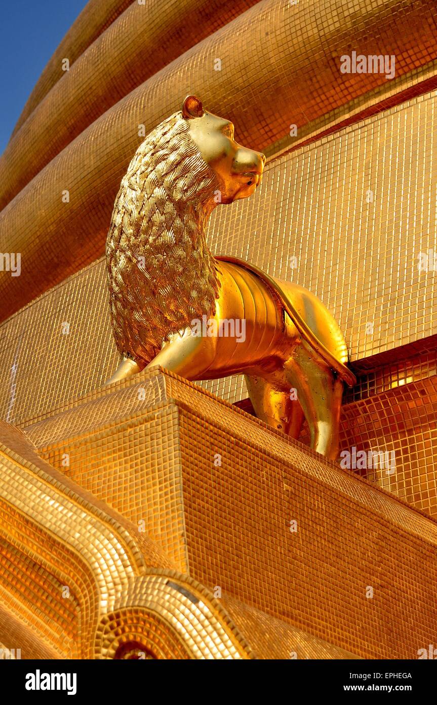 Bangkok, Thaïlande : lion doré se tient sur une corniche près de la base du grand chedi doré au Royal Wat Boworniwet Banque D'Images Bangkok, Thaïlande : lion doré se tient sur une corniche près de la base du grand chedi doré au Royal Wat Boworniwet Banque D'Images