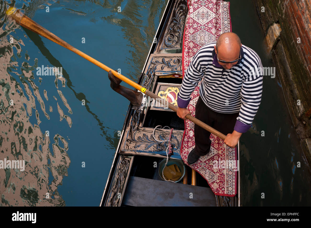 Venise, Italie - 24 avril 2013 : Gondolier en chemise rayée classique gondole traditionnelle pousse le long les eaux d'un canal. Banque D'Images