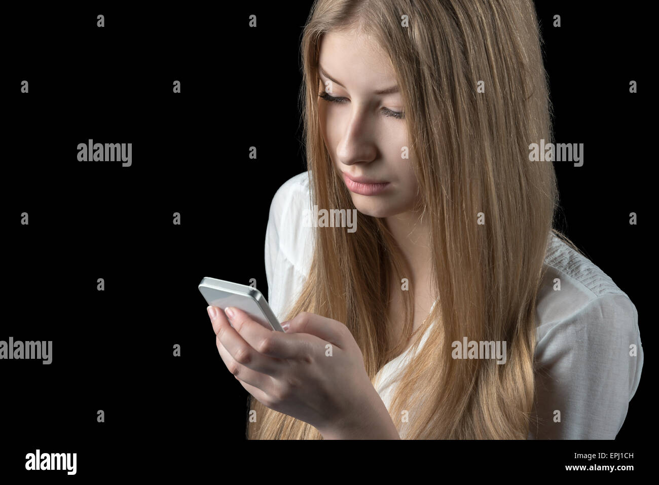 Charmante fille se sent déprimé après la lecture de mauvais sms sur son téléphone cellulaire. Isolé sur le noir. Banque D'Images