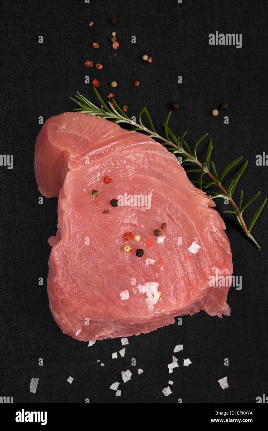 Steak de thon cru avec du romarin frais herbe, Flocons de sel et poivre en grains colorés isolé sur fond noir vue d'en haut. Culinary Banque D'Images