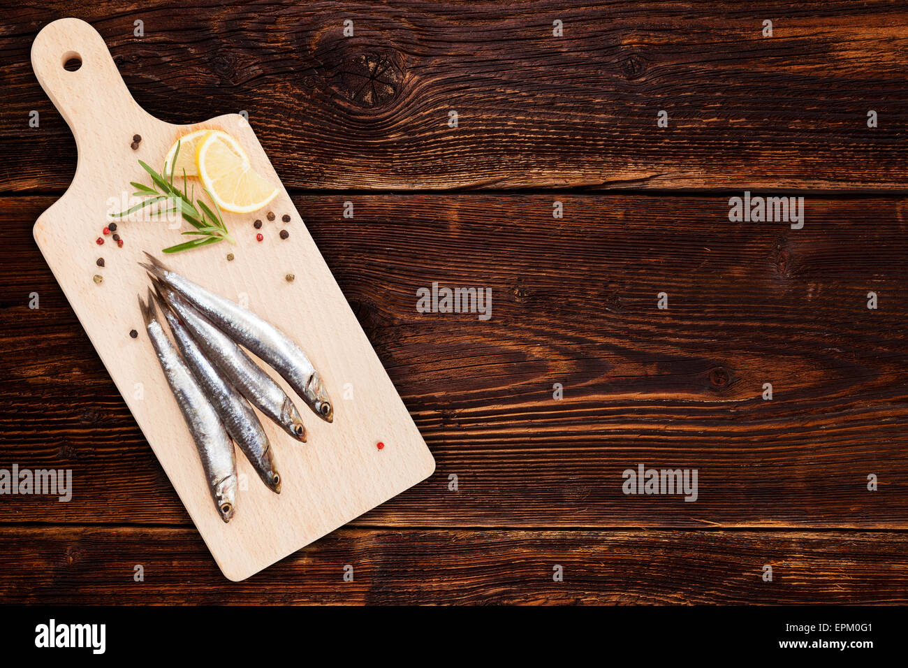 De délicieuses sardines fraîches sur cuisine en bois avec du citron, romarin et poivre colorés sur fond de bois Banque D'Images