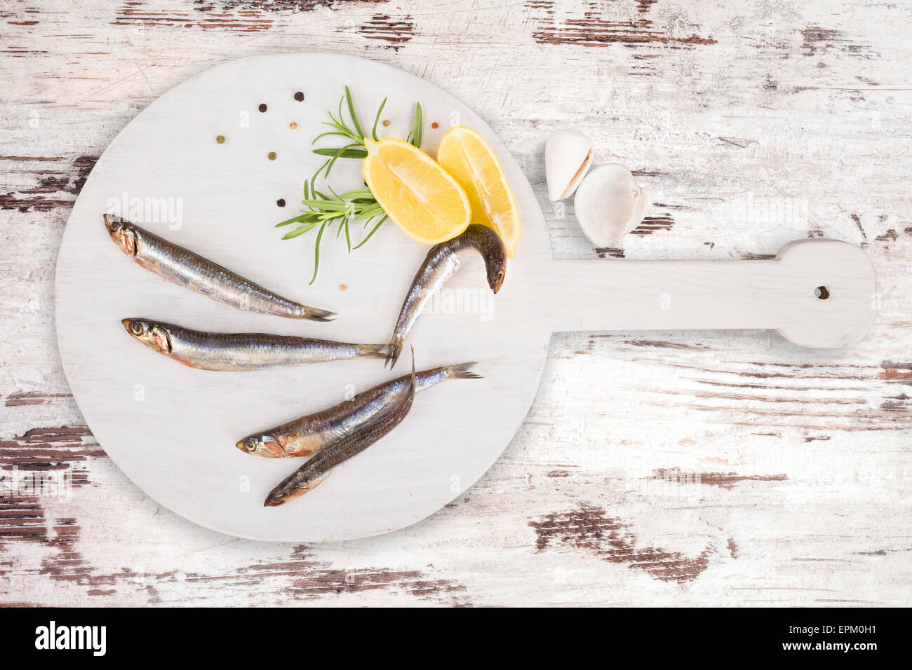 De délicieuses sardines fraîches sur cuisine en bois avec du citron, romarin et poivre colorés sur fond blanc en bois texturé Banque D'Images
