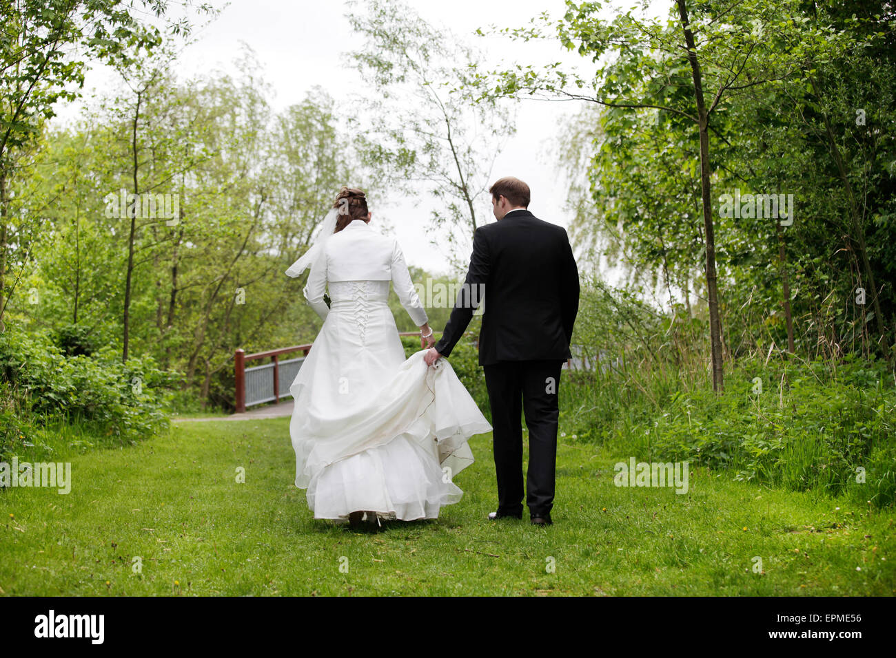 Une mariée dans une robe de mariée blanche à marcher avec son époux dans la nature Banque D'Images