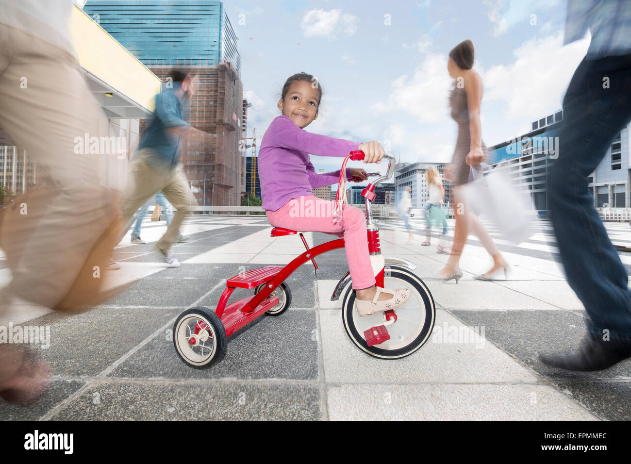 Girl riding un tricycle entre une foule de personnes dans une ville Banque D'Images