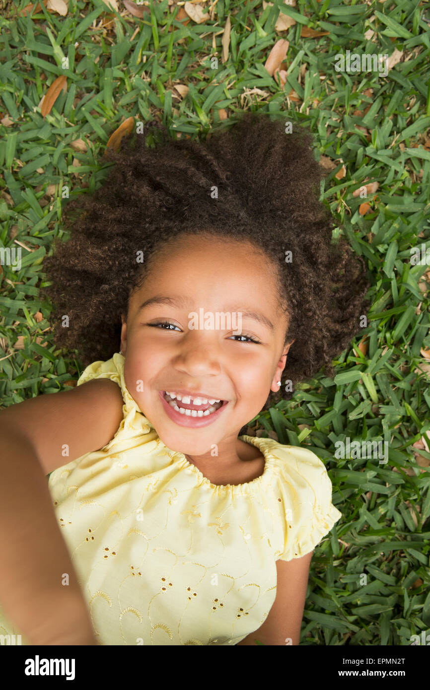 Une jeune fille allongée sur le dos sur l'herbe, souriant et regardant vers le haut. Banque D'Images