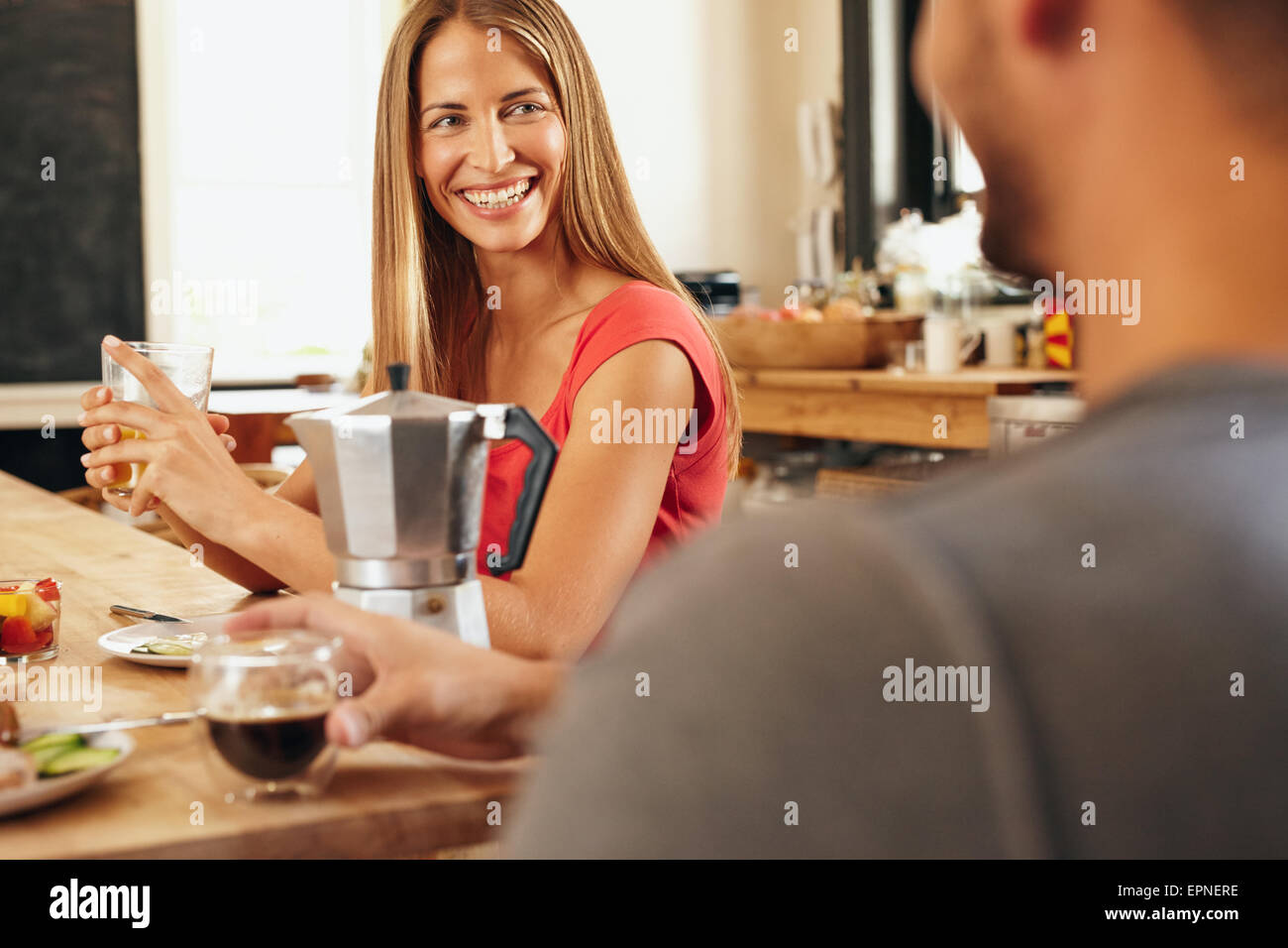 Happy young couple sitting ensemble dans la cuisine et prendre le petit-déjeuner. Souriante jeune femme qui parle avec son petit ami en face Banque D'Images