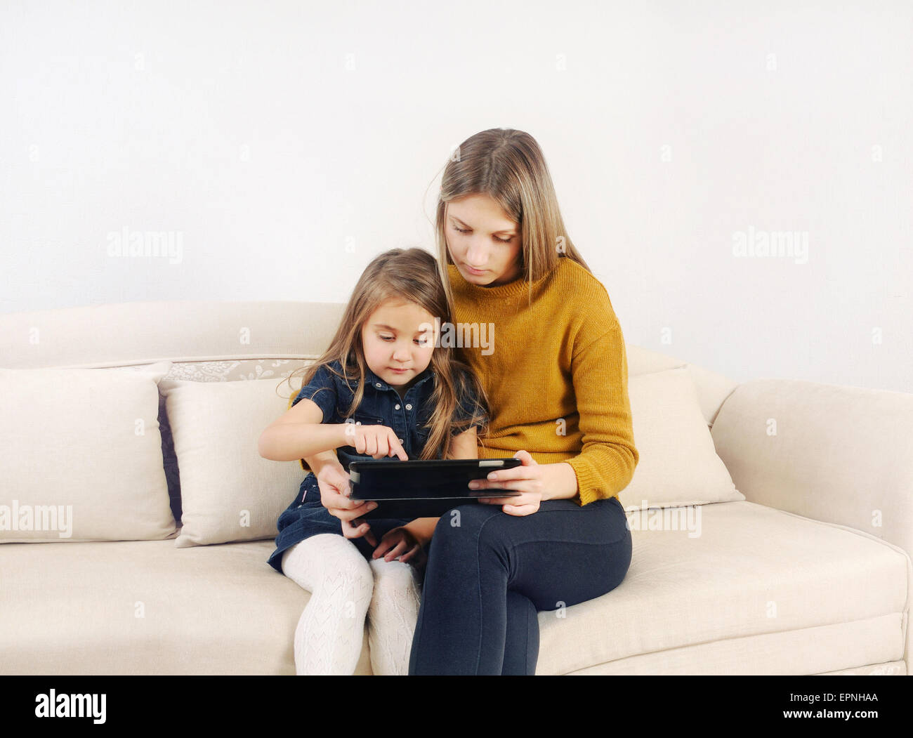 Petite fille avec sa mère à l'aide de tablette sur le canapé à la maison, famille heureuse, technologie concept Banque D'Images