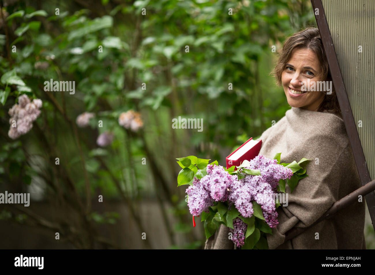 Belle jeune femme avec un bouquet de lilas et un livre dans les mains, à l'air libre parmi la verdure. Banque D'Images