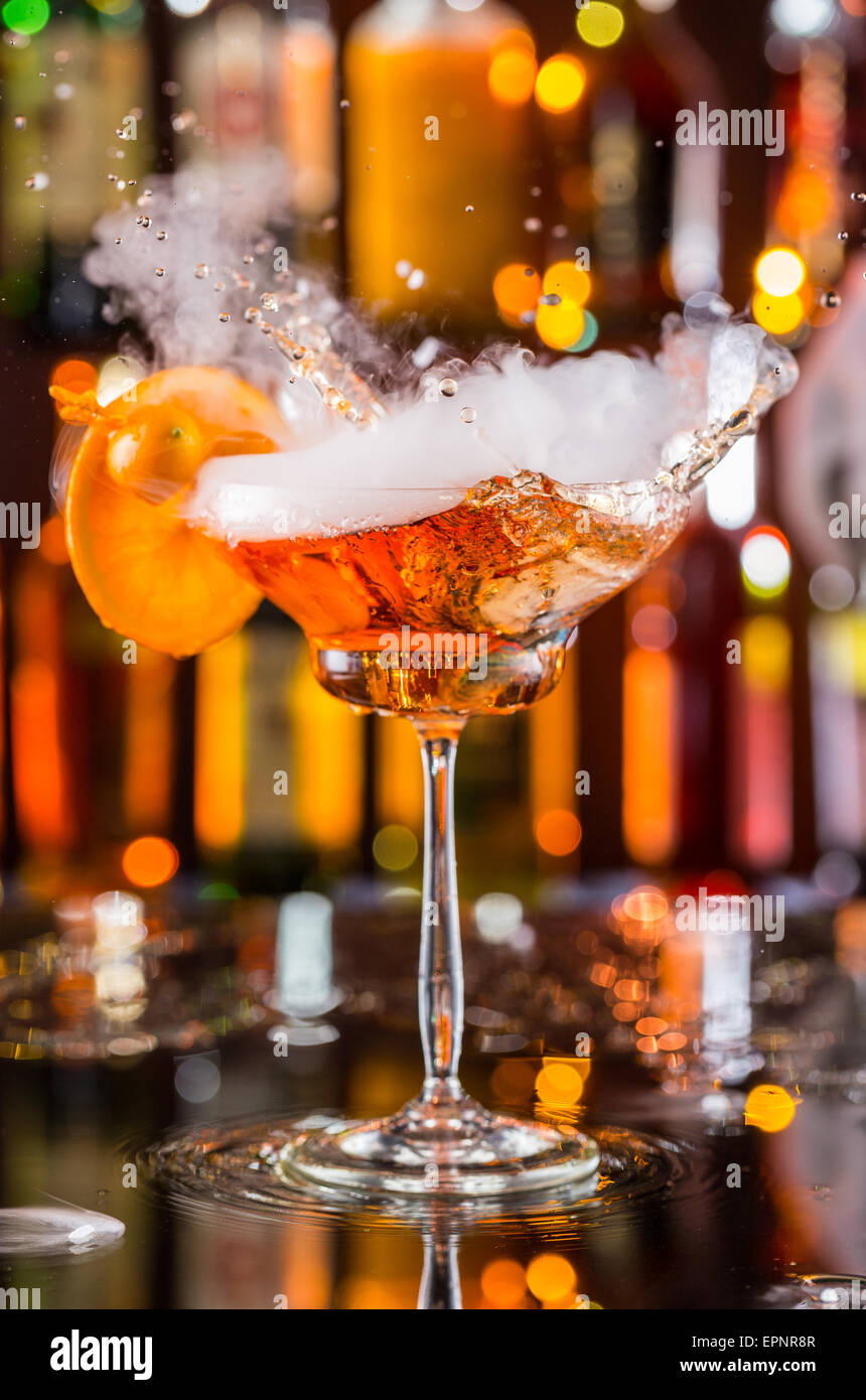 Verre à cocktail avec de la glace sèche effet de fumée et de bruit, servi  sur comptoir bar avec des bouteilles sur fond flou Photo Stock - Alamy