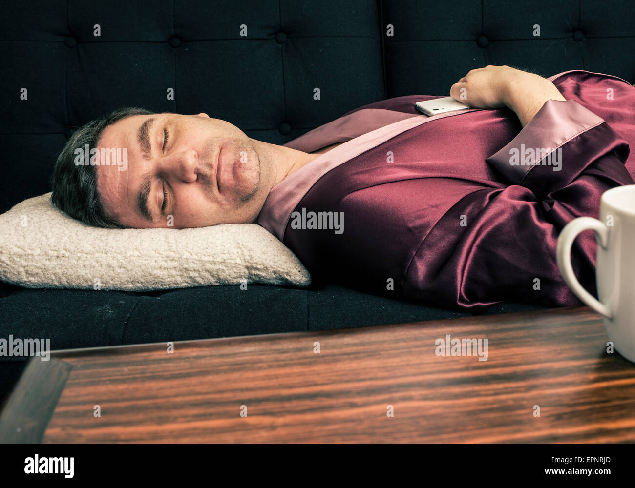 Homme étendu et se reposer sur un canapé à la maison. Il est en train de dormir avec sa tête sur un coussin et tenant un téléphone cellulaire dans les mains. Banque D'Images