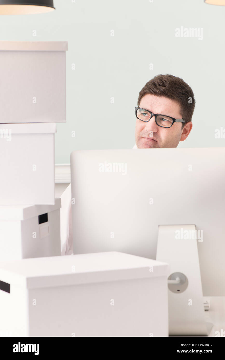 Man avec l'ordinateur de bureau à bureau. Il est entouré par des boîtes blanches utilisées pour le déplacement. Image conceptuelle de l'entreprise Banque D'Images