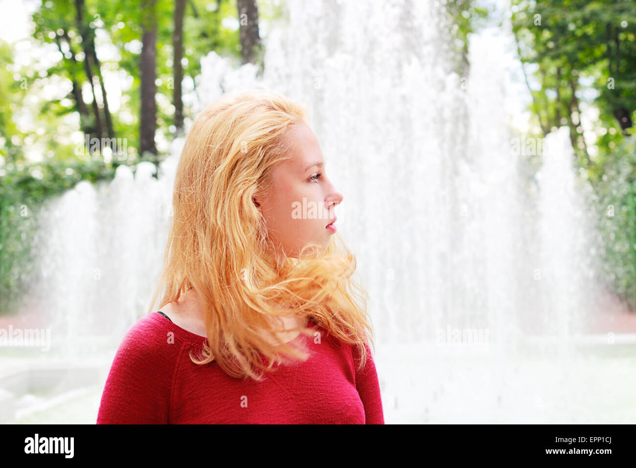 Une jeune fille aux longs cheveux blonds sur un arrière-plan d'une fontaine Banque D'Images