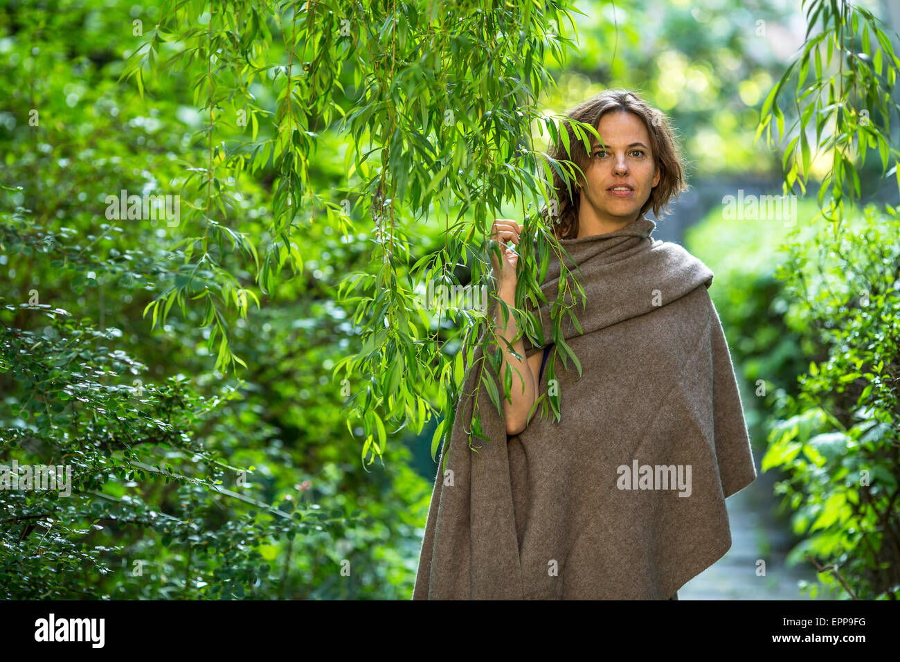 Belle jeune femme en poncho parmi le vert feuillage dans le jardin. Banque D'Images
