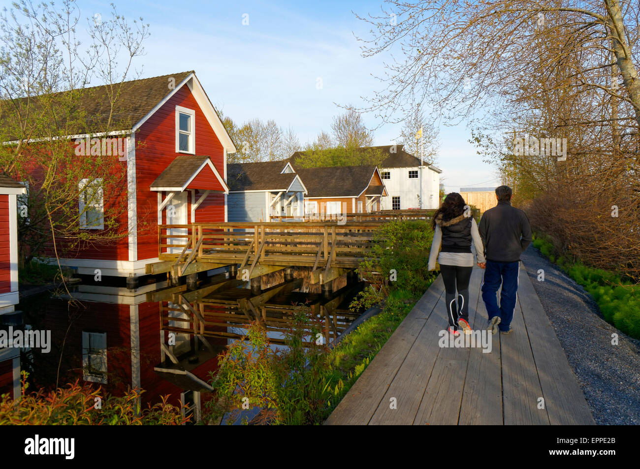 Jeune couple en passant devant des maisons sur pilotis en bois restauré à Britannia, chantier naval du patrimoine, Steveston, Richmond, British Columbia, Canada Banque D'Images