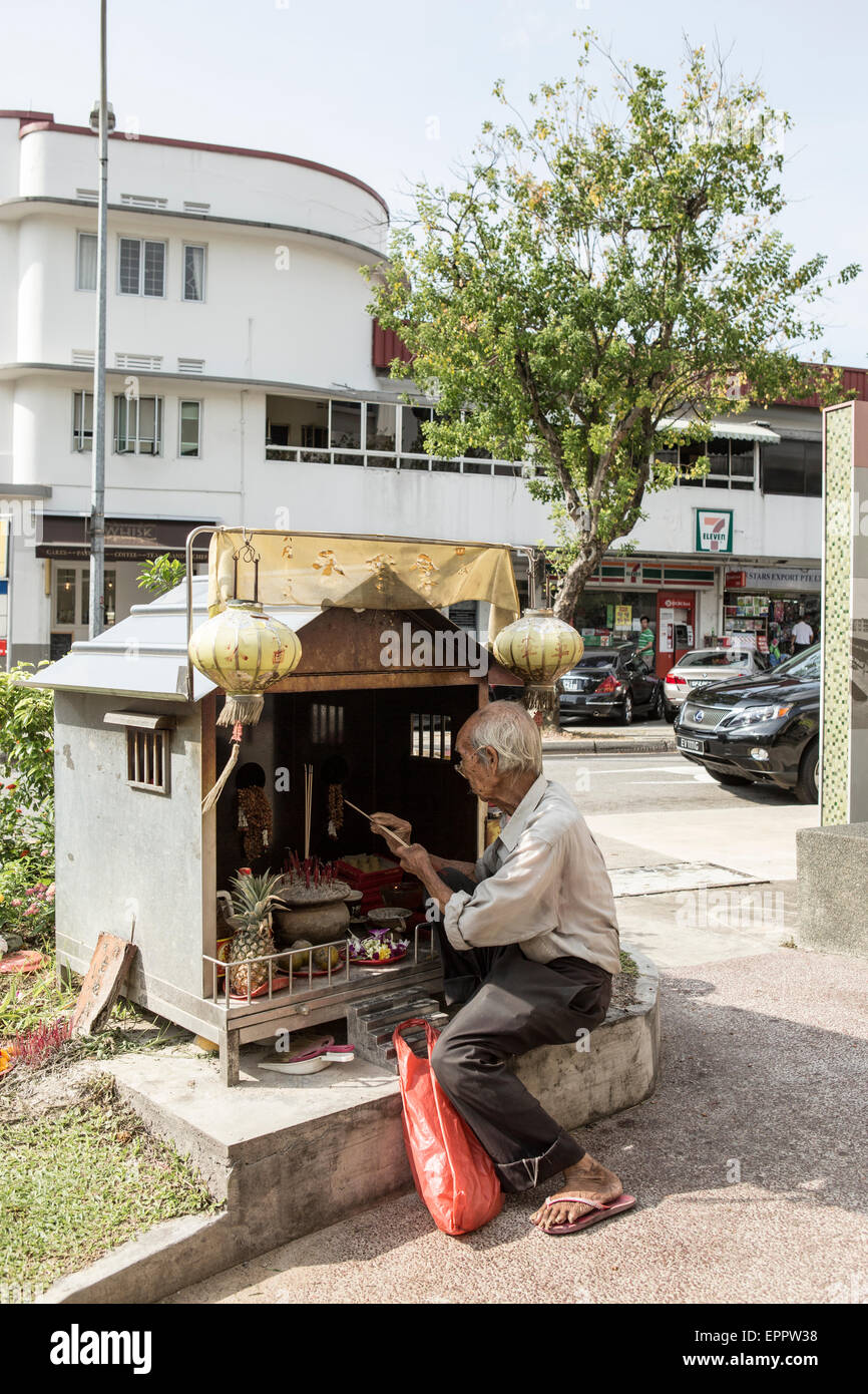 Un homme s'allume de l'encens dans un petit côté route de culte dans la région de Tiong Bahru Singapour. Banque D'Images