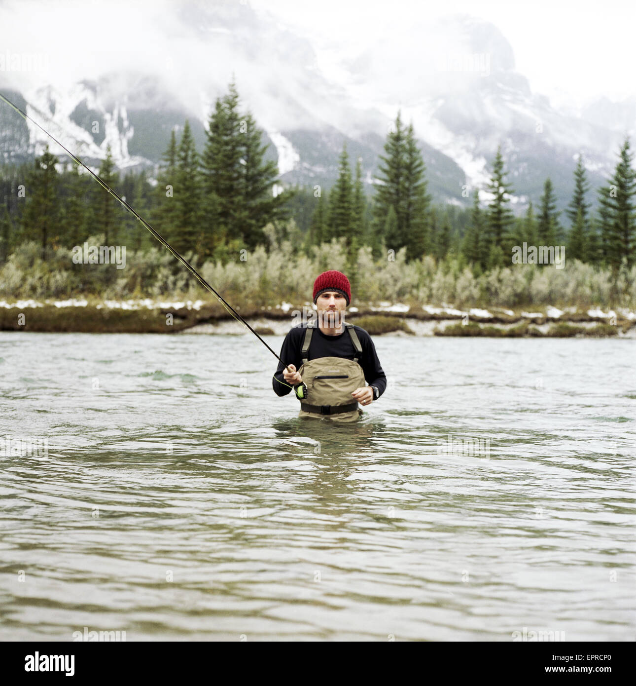 Un homme avec une canne à pêche de mouche pose pour un portrait dans la rivière Bow dans le parc national Banff. L'Alberta, Canada. Banque D'Images