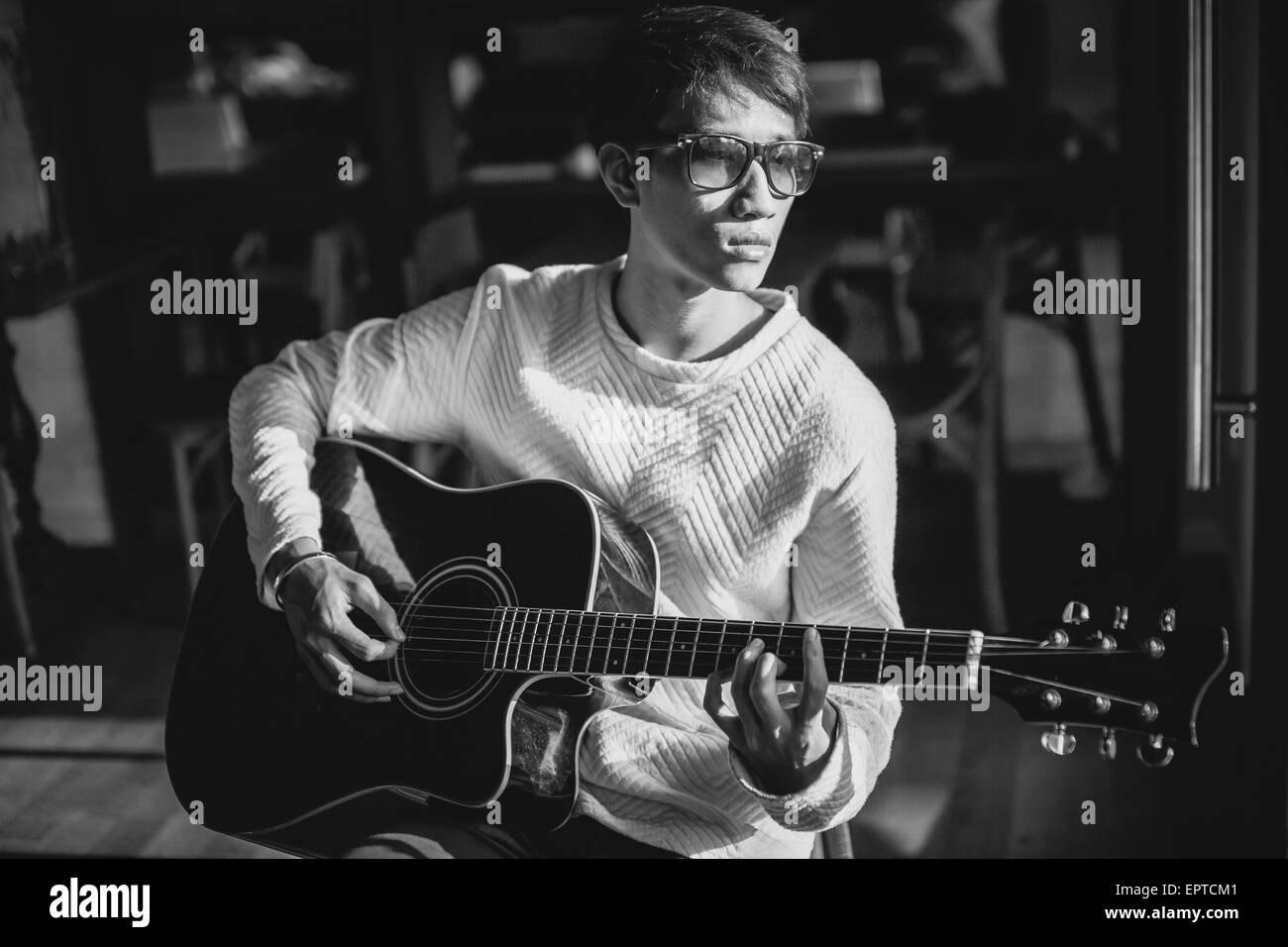 Bel homme artiste guitariste asiatique jouer la guitare acoustique dans le café. Le noir et blanc Banque D'Images