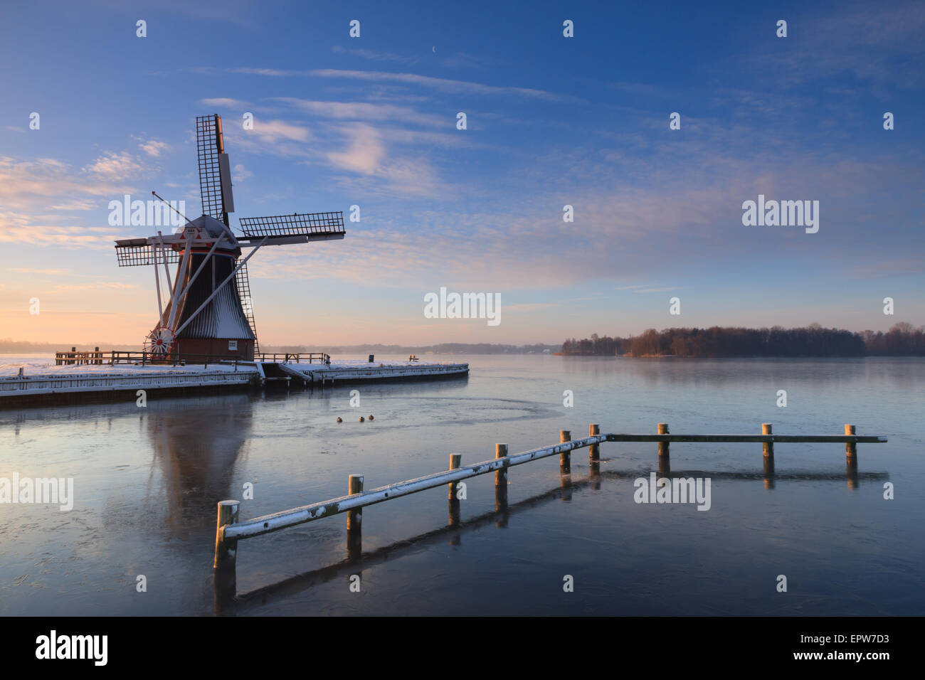 Moulin à vent hollandais à un lac au cours d'un lever du soleil d'hiver. Banque D'Images