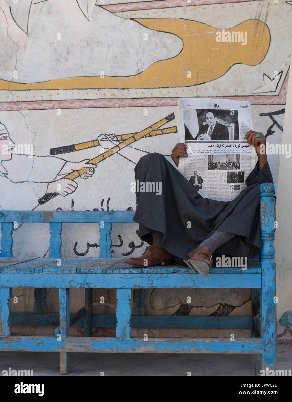 Homme portant une djellaba lire un journal à l'extérieur d'un atelier d'albâtre recouvert de peintures traditionnelles. Louxor, Égypte Banque D'Images