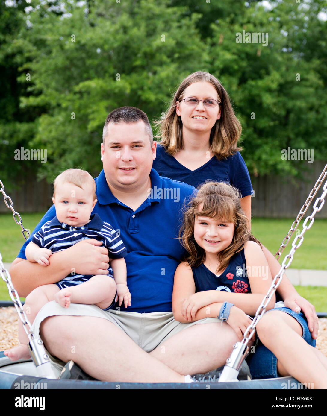 Family posing sur une balançoire à une aire de stationnement en plein air Banque D'Images