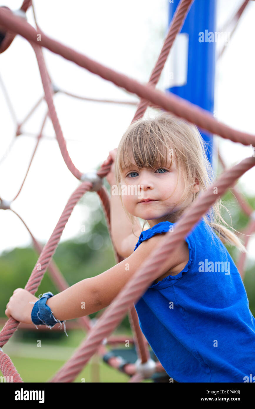 Les jeunes Blue Eyed Girl joue sur une corde en plein air Jungle gym à une aire de stationnement Banque D'Images
