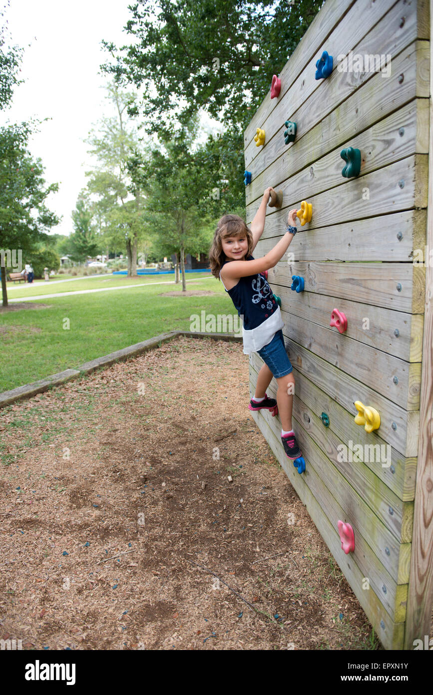 Jeune fille grimpe un mur de pierre dans un parc de jeux extérieur Banque D'Images