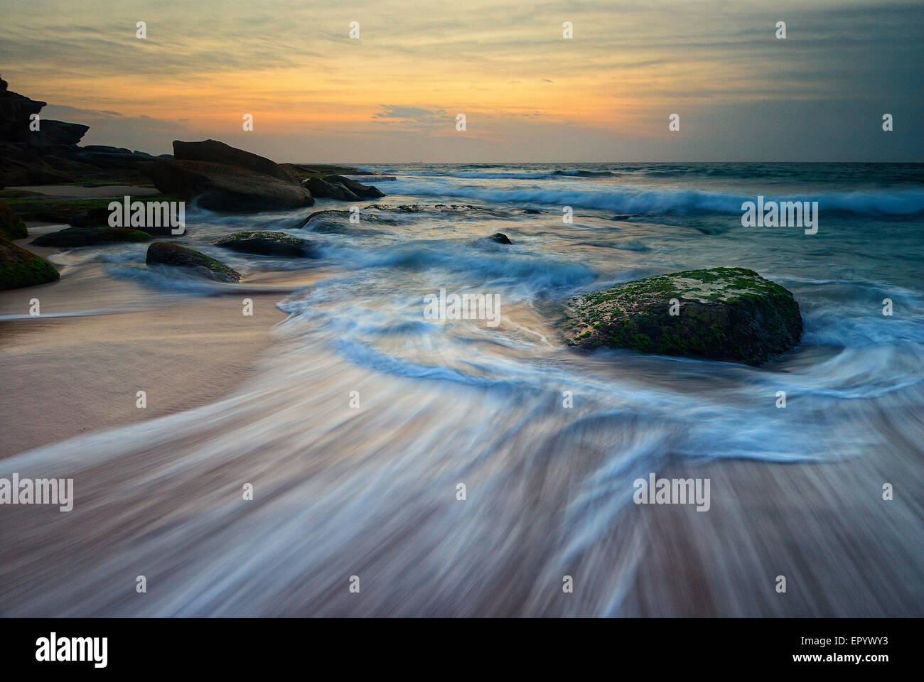 Seascape lever du soleil dans une famille mossy roche avec une vague qui coule autour d'elle Banque D'Images