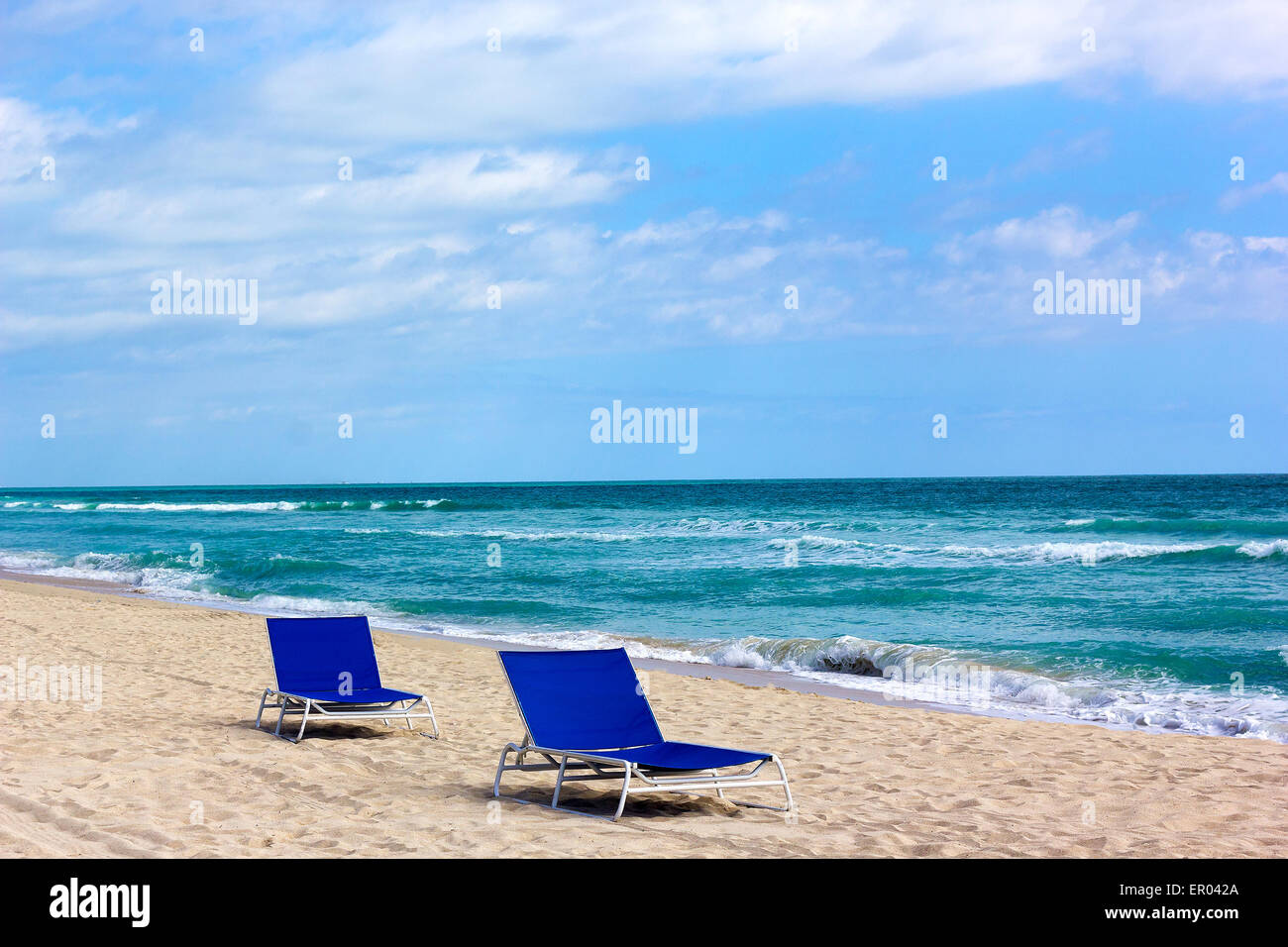 Chaises bleu solitaire sur une plage de l'océan de sable. Chaises de plage se tourna dans la direction de soleil du matin. Banque D'Images