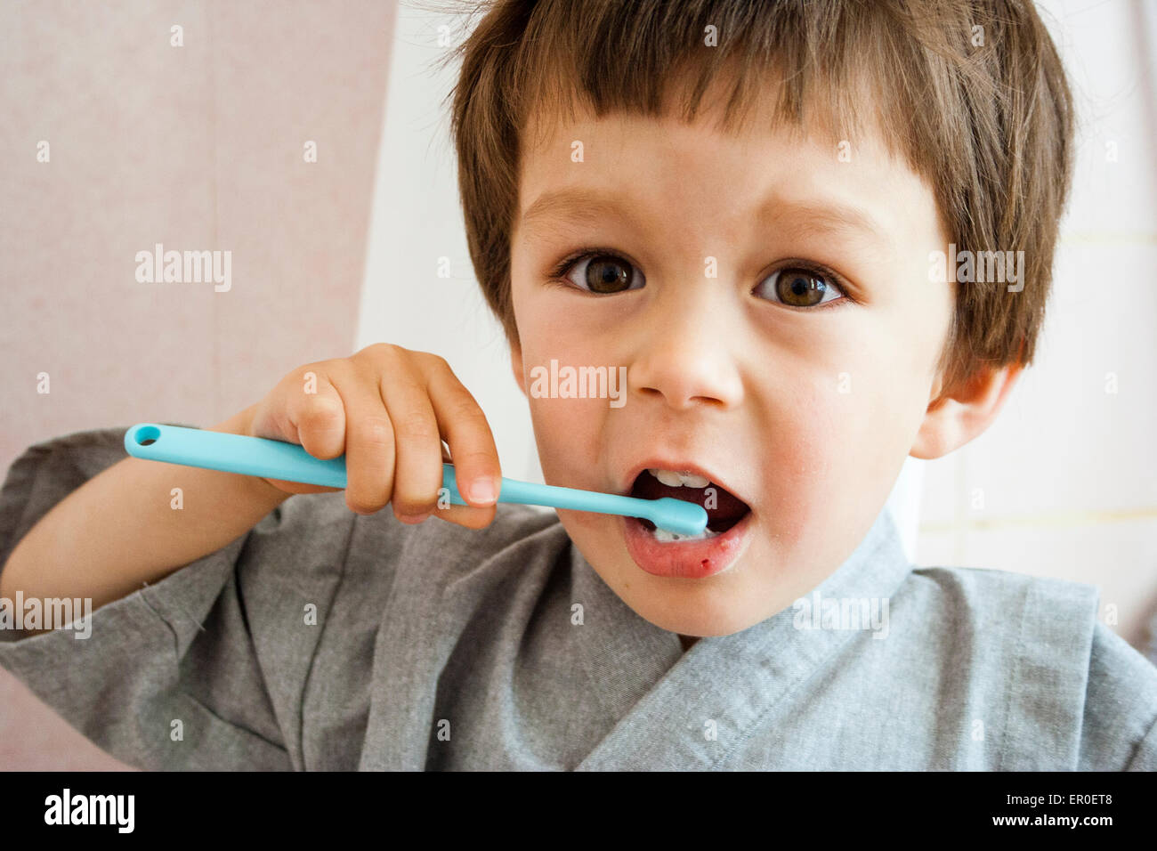 Gros plan sur un jeune enfant, un garçon, se brosser les dents avec une brosse à dents pour enfant tout en regardant le spectateur. Intérieur. Vue de la tête et des épaules. Lumière naturelle. Banque D'Images