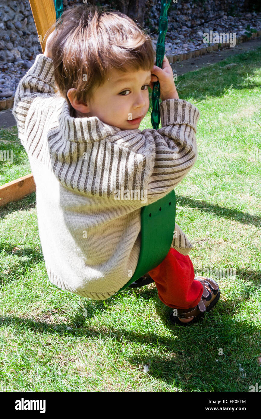 Petit enfant, garçon, 3-4 ans, assis sur une balançoire de jardin. Vu de  derrière, il regarde de l'arrière-plan vers le spectateur. Gilet épais  Photo Stock - Alamy