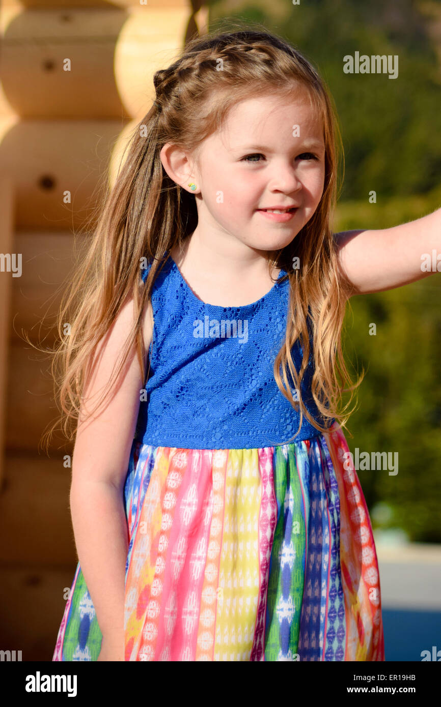 Jolie 4 ans, fille en robe bleu coloré sur log cabin. Banque D'Images