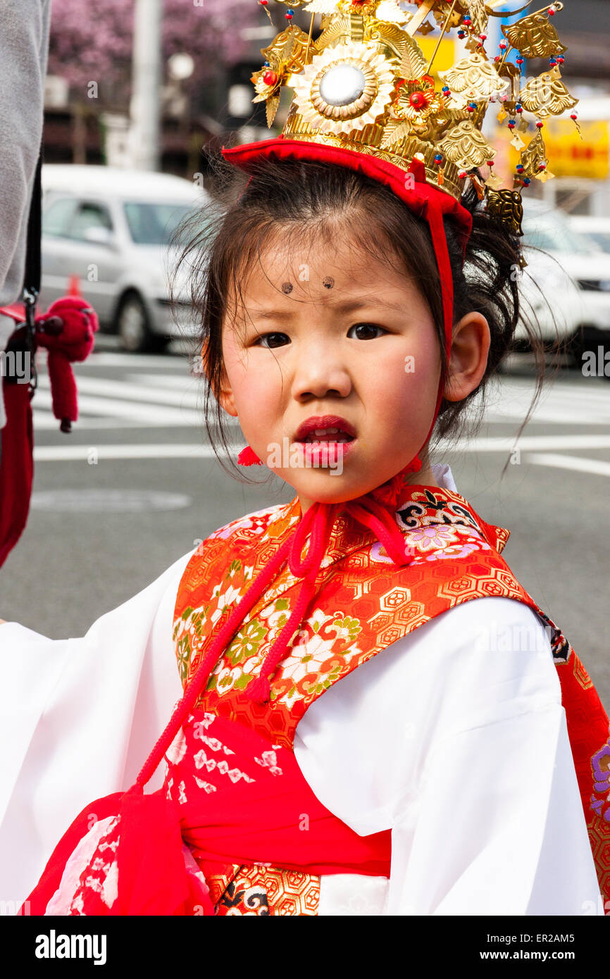 Jeune enfant, fille, portant une veste rouge avec des manches en soie blanche et une couronne d'or marchant dans le défilé de Genji au printemps à Tada, Japon. Contact avec les yeux. Banque D'Images