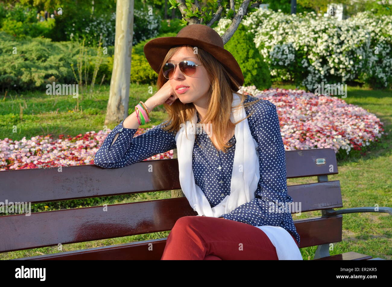 Pensive fille assise sur un banc de parc portant un chapeau brun Banque D'Images