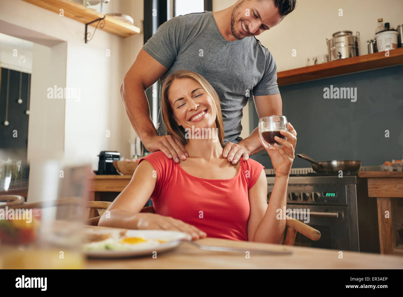 Happy young woman holding tablet petit déjeuner tasse de café d'obtenir un massage de l'épaule de son petit ami. Jeune couple Banque D'Images