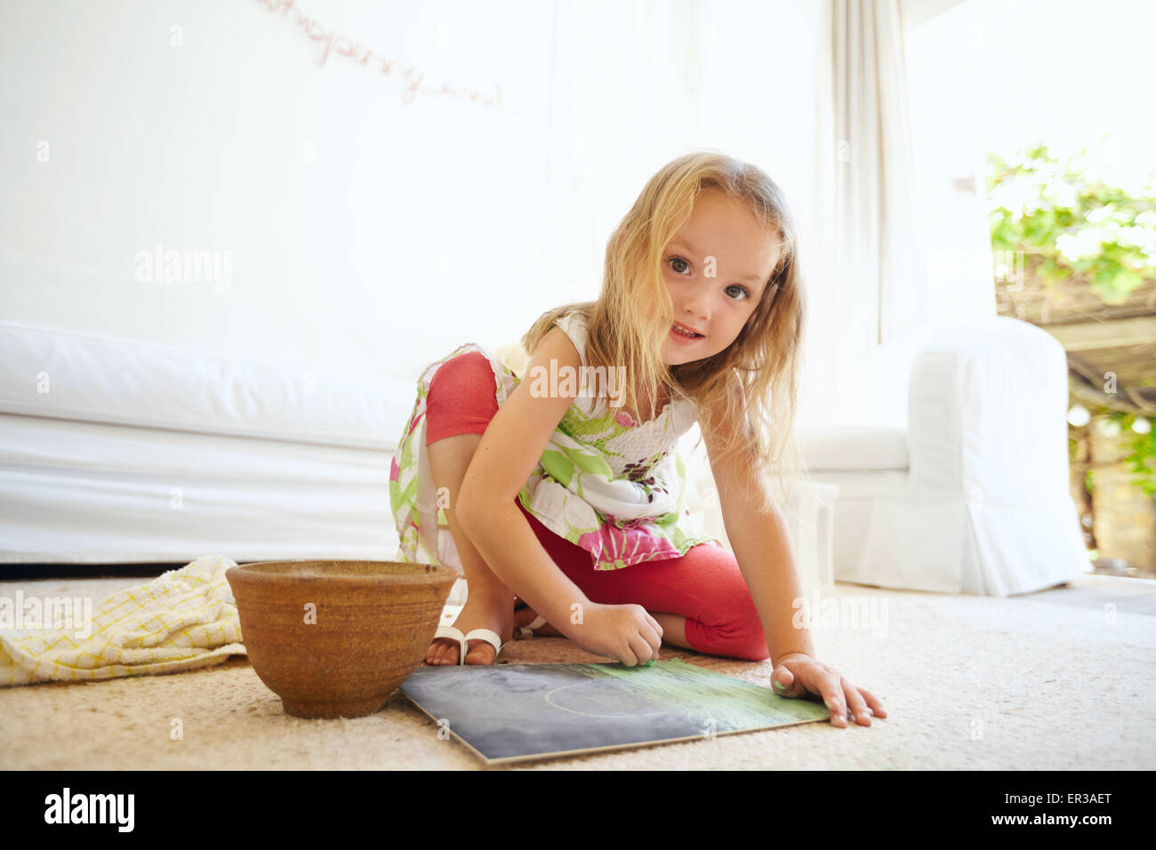 Portrait de petite fille innocente la peinture d'une photo. Assis sur le plancher d'écolière de coloration en souriant. Banque D'Images